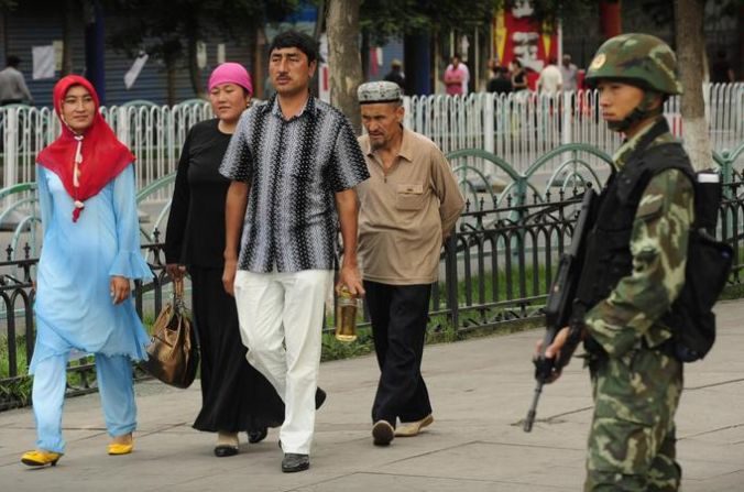 Un agent de police paramilitaire chinoise observe une famille des Ouïghours. (PETER PARKS / AFP / Getty Images)