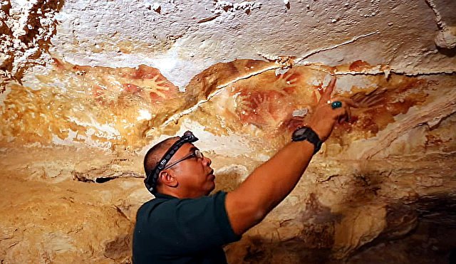 L'archéologue indonésien Muhammad Ramli de l’"Association de préservation de la réserve culturelle" explique comment les couleurs des peintures murales ont changé au cours des dernières décennies. Photo: YouTube Capture d'écran / vidéo nature.