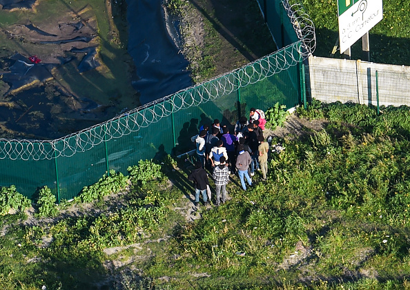 Vue aérienne montrant les migrants se rassembler le 14 octobre 2017 près de la clôture d'une station-service, près de l'ancien camp de migrants «la Jungle» qui a été évacué il y a 12 mois à Calais. Un an après l'évacuation du camp de migrants, le nombre de cambriolages nocturnes dans les camions en direction de la Grande-Bretagne a été divisé par trois, alors que les intrusions dans le tunnel reliant la France et la Grande-Bretagne ont cessé. Les manifestations massives de combats qui nécessitaient des interventions policières ont également cessé.  (FRANCOIS LO PRESTI / AFP / Getty Images)