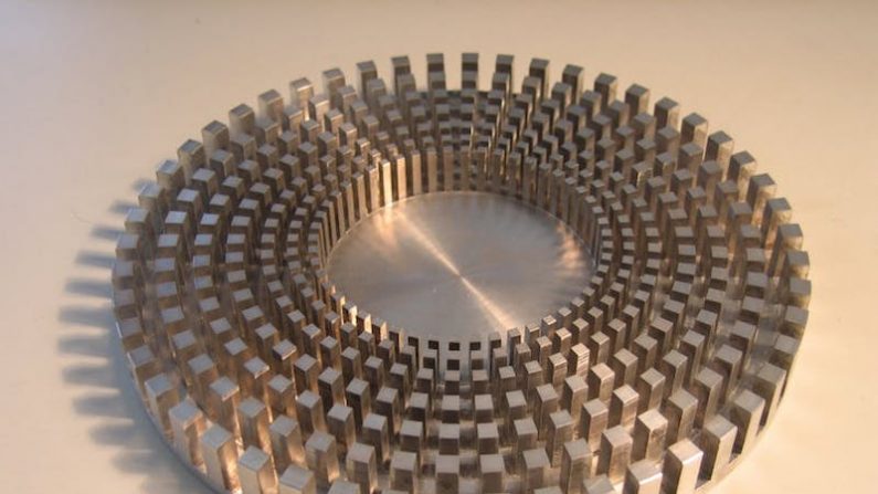 Cape d'invisibilité pour les vagues ou bouclier anti-tsunami. Cette structure hérissée de petits plots, est usinée dans un disque d'aluminium de 20 cm de diamètre. Son rayon extérieur est de 10 cm. Le métamatériau utilisé se comporte comme un fluide anisotrope forçant les vagues à contourner la zone centrale. Ce type de structure pourrait constituer une nouvelle voie pour préserver certaines zones côtières de l'érosion, ou protéger des installations maritimes, telles que les plateformes pétrolières, des lames de fond. (Stefan Enoch/CNRS)