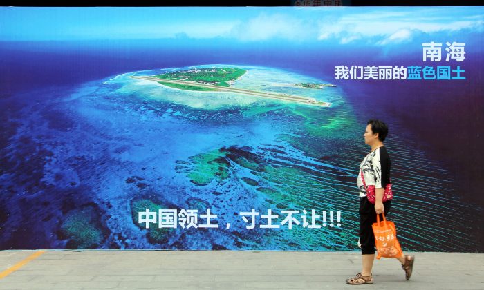 Une Chinoise passe devant une affiche avec l’image de la mer de Chine méridionale et le slogan « Territoire chinois, ne jamais céder un pouce de notre terre » dans une rue de Weifang, province du Shandong, le 14 juillet 2016. La Chine envisage de créer deux tribunaux maritimes internationaux sous son contrôle pour justifier ses propres revendications maritimes, y compris celles dans la mer de Chine méridionale qui ont été jugées illégales par Cour permanente d'arbitrage de La Haye en juillet 2016. Le 15 juillet, quelques jours après que cette Cour internationale a rejeté les revendications de Pékin dans ces eaux stratégiquement vitales, les médias officiels chinois ont annoncé que la Chine pourrait construire des centrales nucléaires mobiles dans la mer de Chine méridionale. (STR / AFP / Getty Images)