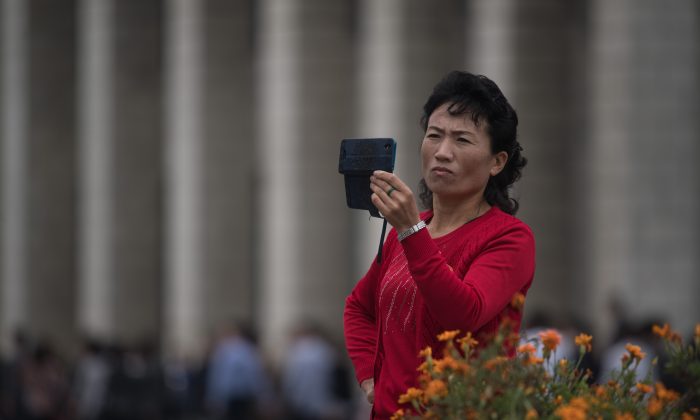 Une femme se sert d'un téléphone portable pour enregistrer des séquences vidéo alors qu'une troupe de propagande agite des drapeaux devant la gare centrale de Pyongyang, le 27 septembre 2017. (ED JONES/AFP/Getty Images)