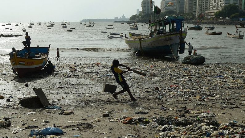 Un Indien joue au cricket sur une plage jonchée de déchets plastiques à Mumbai le 3 juin 2015. Photo PUNIT PARANJPE / AFP / Getty Images.