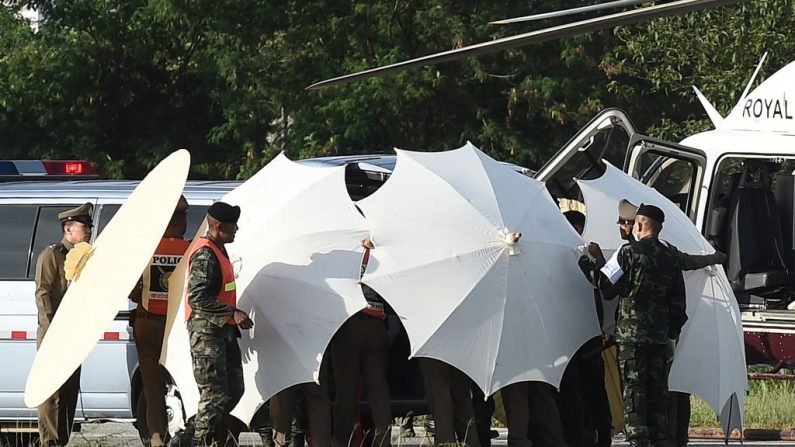 La police et le personnel militaire utilisent des parapluies pour couvrir une civière près d'un hélicoptère et une ambulance dans un aéroport militaire de Chiang Rai le 9 juillet 2018.  Photo LILLIAN SUWANRUMPHA/AFP/Getty Images.