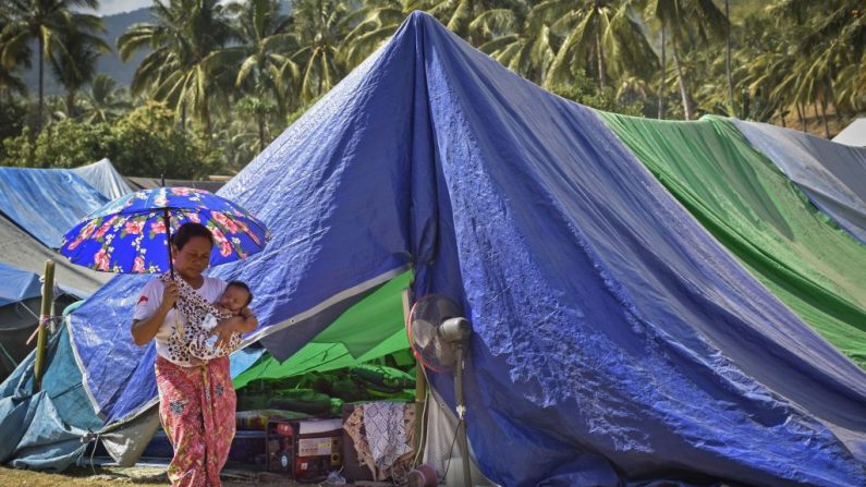 Une femme indonésienne porte un bébé et passe devant des tentes dans un abri temporaire pour les habitants touchés par le séisme. Les victimes du séisme sur l'île indonésienne de Lombok, des corps sont encore récupérés dans les ruines des bâtiments. Photo : STR / AFP / Getty Images.