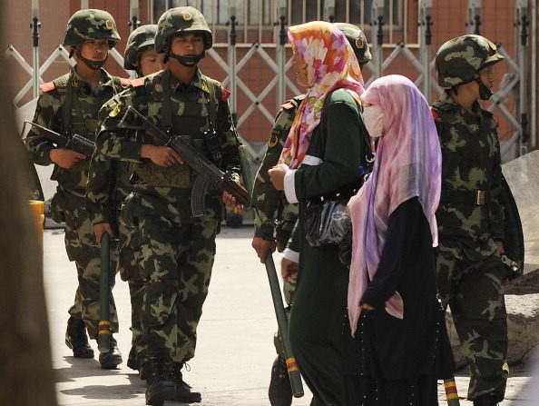 Des femmes ouïgoures de souche musulmane passent devant une patrouille dans la rue d'Urumqi, capitale de la région chinoise du Xinjiang, le 3 juillet 2010, avant le premier anniversaire des violences sanglantes qui ont éclaté entre les Ouïghours de souche et les membres de l'ethnie Han. Photo PETER PARKS / AFP / Getty Images.