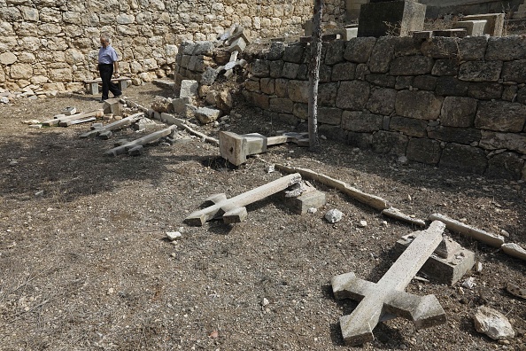 -Le père Antonio Scudu, gardien de l'église Saint-Étienne du monastère salésien de Beit Jamal, examine des croix renversées dans un cimetière qui aurait été vandalisé près de la ville israélienne de Beit Shemesh, à l'ouest de Jérusalem, le 18 octobre 2018. Photo MENAHEM KAHANA / AFP / Getty Images.