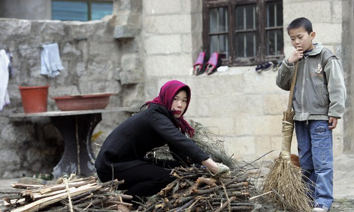 Une agricultrice attachant un bouquet de bois de chauffage pendant que son fils regarde, à l'extérieur de leur maison dans le village Hutou sur l'île de Pingtan. (GOH CHAI HIN/AFP/Getty Images)

