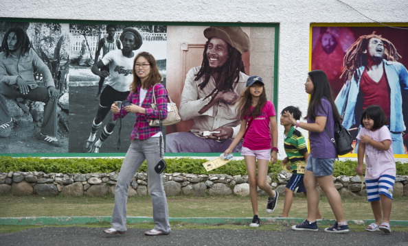 -Les touristes étrangers marchent près d'un mur avec des images de Bob Marley, légende du reggae jamaïcain, son musée à Kingston. La Jamaïque célébrera son 50e anniversaire en tant qu'État indépendant le 6 août 2012. Photo MLADEN ANTONOV / AFP / Getty Images.