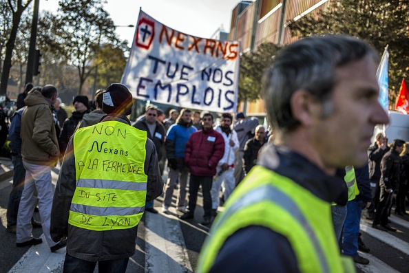 -Un employé du fabricant français de câbles de haute technologie Nexans portant un gilet portant l'inscription "Non à la fermeture de l'usine de Lyon" se tient face à des manifestants portant une banderole portant l'inscription « Nexans tue nos emplois » Photo JEFF PACHOUD / AFP / Getty Images.