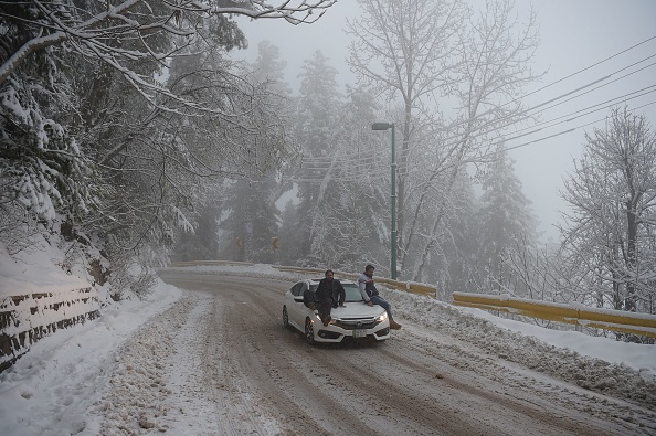 -Des touristes pakistanais sont assis sur une voiture alors qu'ils traversent une rue enneigée lors d'une chute de neige à Murree, à environ 65 km au nord d'Islamabad, le 5 janvier 2019. Photo de AAMIR QURESHI / AFP) / Getty Images.