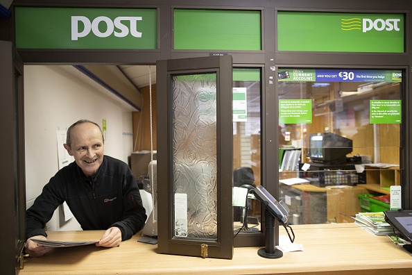 -Le maître de poste James Gallagher pose au bureau de poste, près de la rivière Termon, qui forme la frontière entre l'Irlande du Nord et le Royaume-Uni et divise le village en deux, à Pettigoe, dans le comté de Donegal le 6 mars 2019. Photo de PAUL FAITH / AFP / Getty Images.