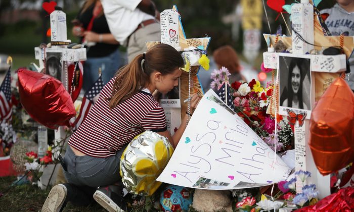 Victoria Seltzer, 11 ans, écrit un passage sur une croix installée dans un mémorial de fortune devant l'école secondaire Marjory Stoneman Douglas en mémoire des 17 personnes tuées le 14 février à Parkland, Floride, le 21 février 2018. La police a arrêté Nikolas Cruz, un ancien élève de 19 ans, pour avoir tué 17 personnes au lycée. (Joe Raedle/Getty Images,)