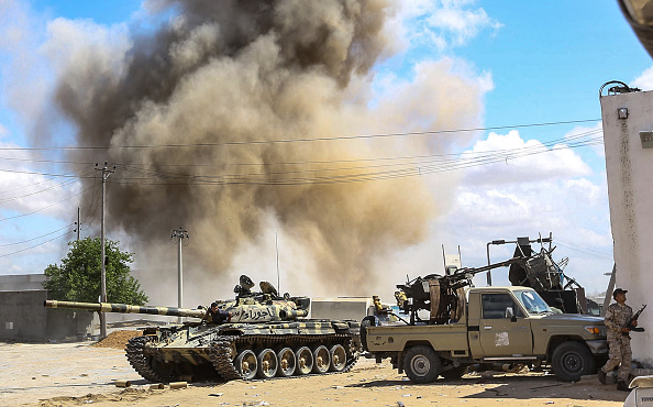 -Cette photo prise le 12 avril 2019 montre un nuage de fumée s'élevant d'une frappe aérienne derrière un char et des dispositifs techniques appartenant aux forces fidèles au gouvernement libyen lors des affrontements dans la banlieue de Wadi, à environ 30 kilomètres au sud de la capitale Tripoli. Photo de Mahmud TURKIA / AFP/ Getty Images.