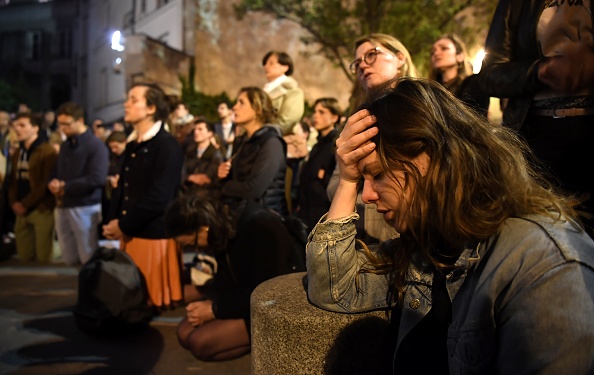 Les gens s'agenouillent sur le trottoir en priant devant les flammes qui engloutissent la cathédrale Notre-Dame à Paris le 15 avril 2019.       (Photo : ERIC FEFERBERG/AFP/Getty Images)