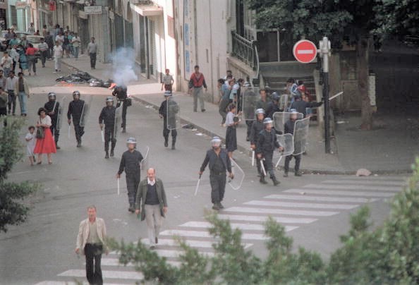 -Des policiers anti-émeute se déploient dans les rues d'Alger alors que l'un d'eux (derrière) tire des gaz lacrymogènes. Les forces de sécurité ont abattu au moins 25 personnes au cours de cette manifestation. Photo should read / AFP / Getty Images.