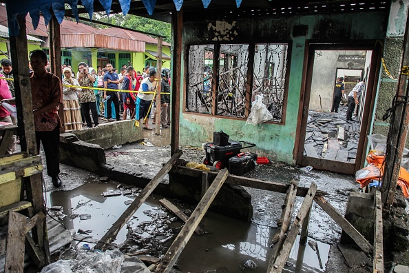 -Des spectateurs se rassemblent devant une maison incendiée qui faisait alors office d’usine d’allumettes à Binjai le 21 juin 2019. Au moins 30 personnes, dont plusieurs enfants, ont été tuées. Photo par Ivan Damanik / AFP / Getty Images.