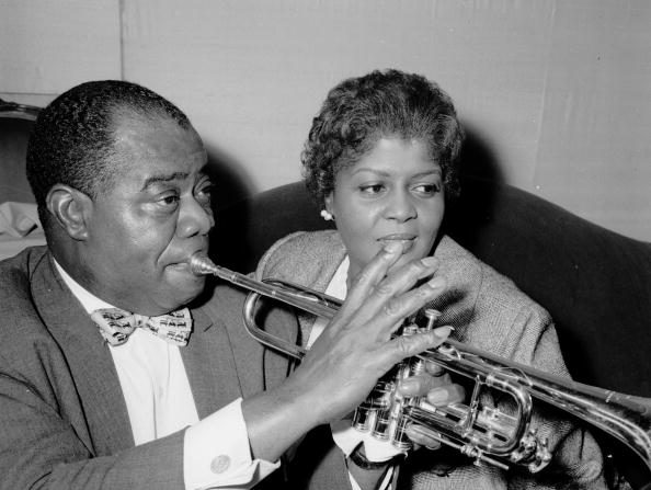 -Le trompettiste et chanteur de jazz américain Louis Armstrong (1898 1971) joue de la trompette alors qu'il est assis avec son épouse Lucille au Mayfair Hôtel, à Londres. Photo de William Vanderson / Fox Photos / Getty Images.