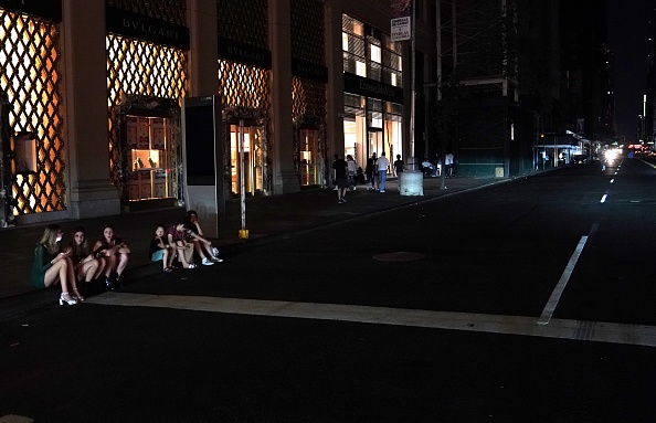 -Des personnes sont assises sur le trottoir lors d'une coupure de courant majeure dans certaines parties de la ville de New York le 13 juillet 2019. Les stations de métro ont sombré dans l'obscurité et les panneaux publicitaires de Times Square ont soudainement disparu lorsque la panne d'électricité de Manhattan, à New York, s'est produite samedi. Photo par TIMOTHY A. CLARY / AFP / Getty Images.