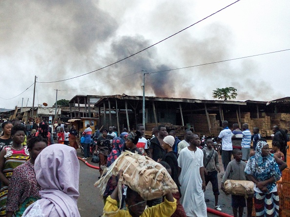 -Des gens passent devant le marché de Bouaké, dans le centre de la Côte d'Ivoire, le 27 août 2019, alors que la fumée monte après l'incendie qui s'est déclaré. Photo de STR / AFP / Getty Images.