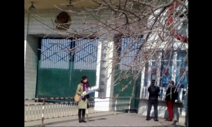 En 2018, Ge Xiulan se tient devant la prison de Binhai avec des fleurs pour son mari incarcéré. Les autorités de la prison ne lui ont pas permis de lui rendre visite ce jour-là. (Minghui.org)