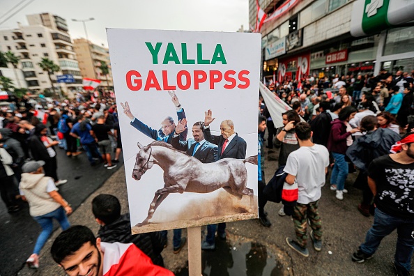 Une pancarte représentant le président libanais Michel Aoun, le Premier ministre Saad Hariri et le président du Parlement, Nabih Berri, les saluant derrière un cheval au galop élevé lors d'une manifestation le septième jour de protestation contre les augmentations d'impôts et la corruption officielle à Zouk Mosbeh, au nord de la capitale Beyrouth, le 23 octobre 2019. (Photo : JOSEPH EID/AFP via Getty Images)