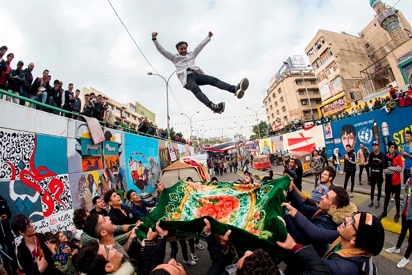 -Un jeune manifestant irakien est projeté en l'air par d'autres manifestants alors que les rassemblements anti-gouvernementaux se poursuivent sur la place Tahrir à Bagdad, le 3 décembre 2019. Les manifestations sont transformées en pièces de théâtre, peintures, poèmes et littérature. La place Tahrir est devenue un centre artistique, un espace rare pour la liberté d'expression dans un pays conservateurs. Photo de HUSSEIN FALEH / AFP via Getty Images.