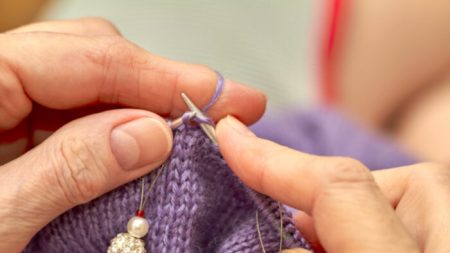 Une femme anonyme de 88 ans tricote des bonnets en laine et les accroche à une clôture dans des sacs plastique pour les enfants qui en ont besoin pendant l’hiver