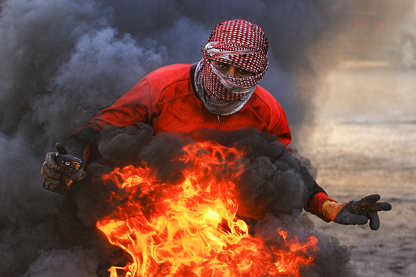 -Un manifestant clignote le geste de la victoire en posant avec des pneus enflammés lors d'une manifestation antigouvernementale contre le nouveau Premier ministre irakien désigné dans la ville sanctuaire centrale de Najaf le 2 février 2020. Photo de Haidar HAMDANI / AFP via Getty Images.