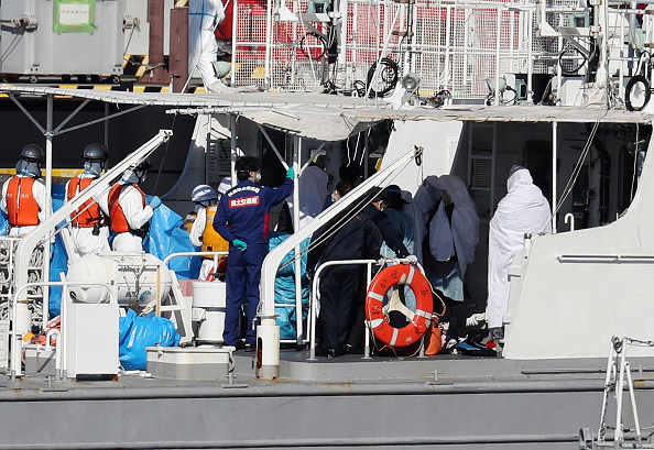 -Des travailleurs sanitaires en tenue de protection transfèrent une personne sous un drap bleu du bateau de croisière Diamond Princess sur un bateau de la Garde côtière japonaise à Yokohama le 5 février 2020. Photo de STR / JIJI PRESS / AFP via Getty Images.