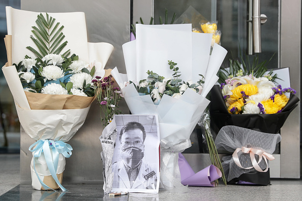 -Une photo de l'ophtalmologiste décédé Li Wenliang est vue avec des bouquets de fleurs à la succursale de Houhu de l'hôpital central de Wuhan, dans la province centrale du Hubei en Chine le 7 février 2020. Un médecin chinois qui a été puni après avoir sonné l'alarme au sujet du nouveau coronavirus chinois est décédé de l'agent pathogène le 7 février 2020. Photo par STR / AFP via Getty Images.