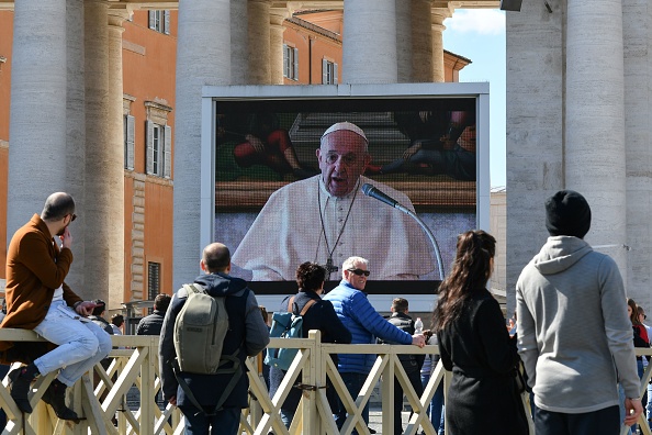 -Les gens regardent un écran diffusant en direct la prière du dimanche de l'Angélus du pape François sur la place Saint-Pierre au Vatican, le 8 mars 2020, après que des millions de personnes ont été placées en quarantaine forcée dans le nord de l'Italie. Photo by ALBERTO PIZZOLI/AFP via Getty Images.