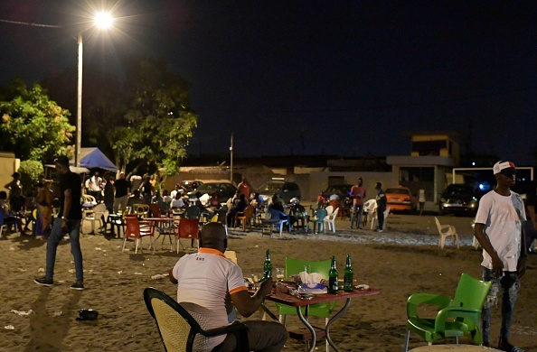 -Les clients se réunissent dans un maquis (bars locaux) dans les quartiers populaires de Yopougon, une grande banlieue d'Abidjan lors d'une opération de police menée par Vincent Toh Bi, le préfet local le 21 mars 2020. Les fameux maquis (bars et restaurants populaires), pour lesquels Abidjan est célèbre la nuit, continuent de se remplir, même s'ils doivent théoriquement réduire la foule pour éviter la propagation du coronavirus en Côte d'Ivoire. Photo par ISSOUF SANOGO / AFP via Getty Images.