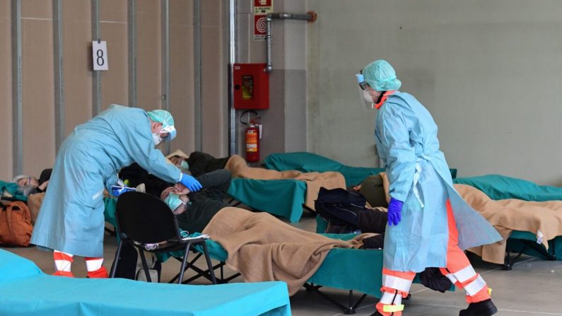 Des employés de l'hôpital portant un masque et un équipement de protection s'occupent d'un patient dans une structure d'urgence temporaire installée à l'extérieur du service des accidents et des urgences de l'hôpital de Brescia, en Lombardie (Italie), le 13 mars 2020. (Miguel Medina/AFP via Getty Images) 