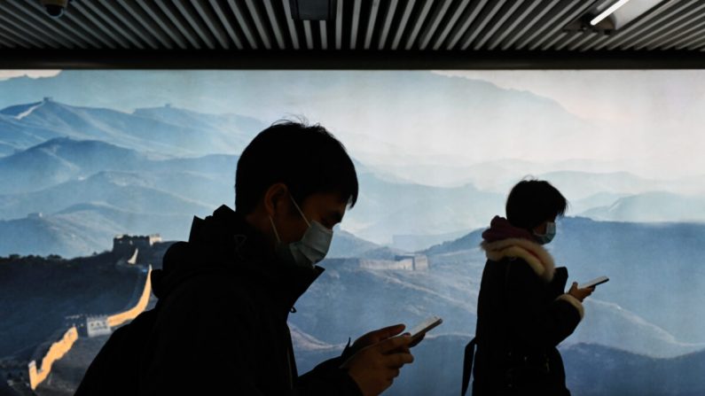 Un homme et une femme portent un masque facial et utilisent leur téléphone portable alors qu'ils entrent dans une station de métro à Pékin le 11 mars 2020. (Wang Zhao/AFP via Getty Images)