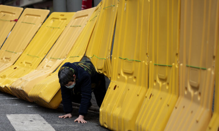 Une femme âgée rampe sous une barricade jaune séparant un complexe résidentiel à Wuhan, en Chine, le 2 avril 2020. (NOEL CELIS/AFP via Getty Images)