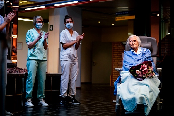 Des travailleurs médicaux applaudissent la patiente belge de 100 ans Julia Dewilde, qui quitte l'hôpital du Bois de l'Abbaye à Seraing, après avoir été traitée avec succès pour COVID-19, le 29 avril 2020. Photo de Kenzo TRIBOUILLARD / AFP via Getty Images.