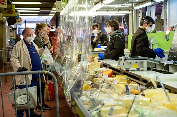 -Les clients, portant des masques de protection, font la queue au comptoir des fromages afin d'être servis derrière un rideau en plastique transparent sur un marché couvert du Perreux-sur-Marne le 19 avril 2020. Photo par BERTRAND GUAY / AFP via Getty Images.