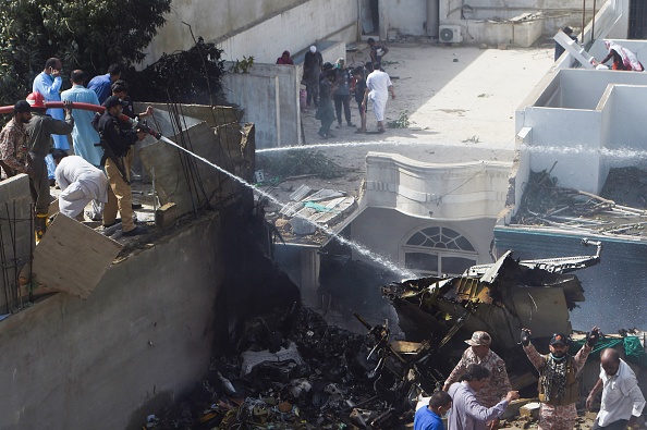 -Des policiers pulvérisent de l'eau sur la partie d'un avion de Pakistan International Airlines après qu'il s'est écrasé dans une zone résidentielle de Karachi le 22 mai 2020. Un avion de passagers pakistanais comptant plus de 100 personnes à bord s'est écrasé dans la ville méridionale de Karachi. Photo par Asif HASSAN / AFP via Getty Images.