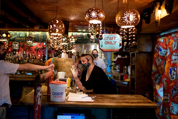 -Un barman portant un masque facial et des gants vérifie l'identité d'un client à Under the Volcano à Houston, Texas, le 22 mai 2020. Photo de Mark Felix / AFP via Getty Images.