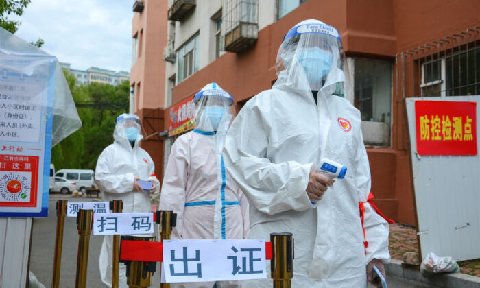 Des employés attendent à l'entrée d'un complexe résidentiel de la ville de Jilin, en Chine, le 25 mai 2020, pour vérifier le permis d'entrée des personnes, contrôler leur température corporelle et scanner leur code de santé. (STR/AFP via Getty Images)