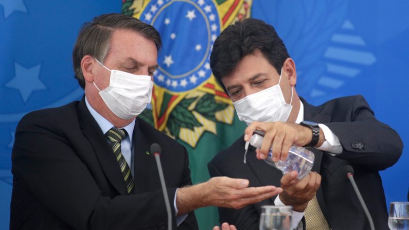 Le ministre brésilien de la Santé, Luiz Henrique Mandetta, donne du gel hydroalcoolique au président Jair Bolsonaro, tous deux munis de masques de protection, lors d'une conférence de presse sur les plans et mesures du gouvernement concernant la crise du virus du PCC, au Palais Planalto à Brasilia, Brésil, le 18 mars 2020. (Andre Coelho/Getty Images)