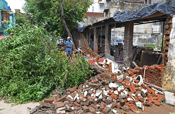 -Un travailleur se tient à côté des débris d'un mur de maison effondré et d'un arbre tombé après de fortes pluies de mousson à Amritsar le 30 juillet 2020. Photo par NARINDER NANU / AFP via Getty Images.