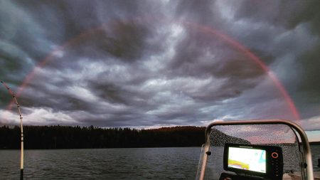 Un spectacle unique : un pêcheur capture une saisissante image d’un arc-en-ciel rouge au-dessus d’un lac finlandais