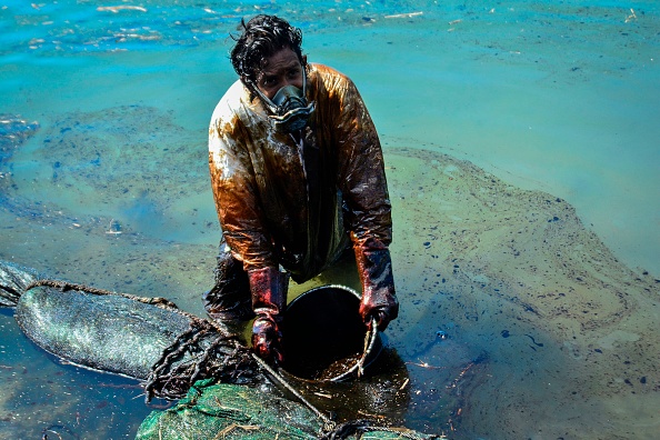 Un homme ramasse le pétrole qui s'est échappé du MV Wakashio, appartenant à une compagnie japonaise mais battant pavillon panaméen. Le navire, qui s'est échoué il y a deux semaines, souille les eaux vierges d'une zone marine écologiquement protégée près du parc marin de Blue Bay, au large des côtes du sud-est de l'île Maurice. (Photo : JEAN AURELIO PRUDENCE/L'Express Maurice/AFP via Getty Images)