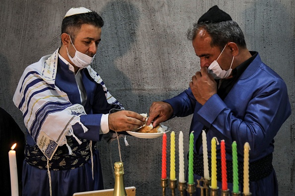 -Un homme juif kurde irakien, rompt une miche de pain avec des membres de la famille pendant leur service de repas de Shabbat dans une maison à Arbil, la capitale de la communauté autonome kurde du nord de l'Irak, le 19 juin 2020. Photo par SAFIN HAMED / AFP via Getty Images.