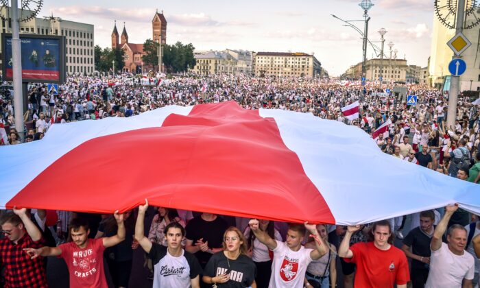 Des partisans de l'opposition biélorusse portent l’ancien drapeau géant blanc-rouge-blanc de la Biélorussie devenu symbole de l’opposition au gouvernement, à Minsk, la Biélorussie, le 16 août 2020. (Sergei Gapon/AFP via Getty Images)