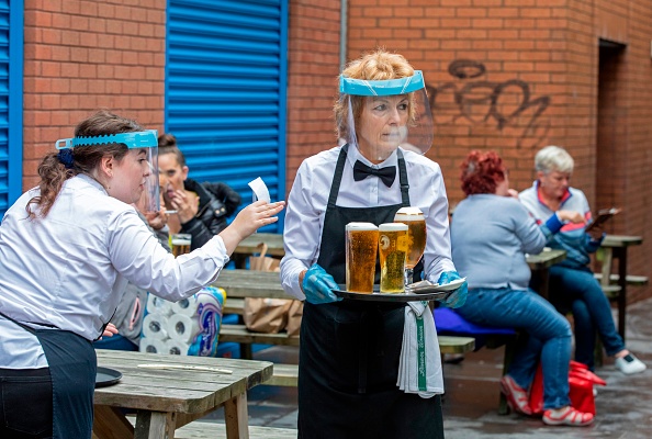 - Le personnel portant des équipements de protection individuelle sous forme d'écrans faciaux et de gants sert les personnes prenant un verre dans le centre-ville de Belfast le 3 juillet 2020. Photo Paul Faith /AFP via Getty Images.