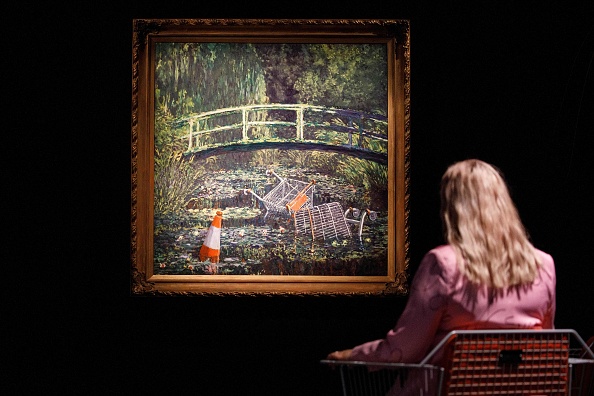 -Un employé de galerie pose avec une œuvre d'art intitulée, Show me the Monet, par l'artiste de rue britannique Banksy pour une vente aux enchères d'art contemporain aux galeries Sotheby's dans le centre de Londres le 16 octobre 2020. Photo de Tolga Akmen / AFP via Getty Images.