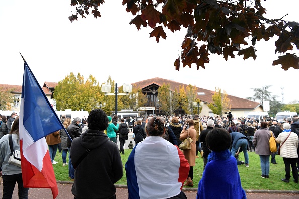 -Des personnes tenant les drapeaux nationaux français se tiennent devant l'entrée d'un collège de Conflans-Sainte-Honorine, le 17 octobre 2020, après qu'un enseignant a été décapité par un agresseur abattu par des policiers. Photo par Bertrand Guay / AFP via Getty Images.